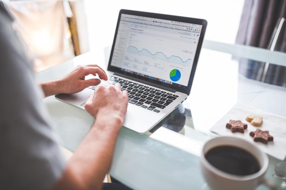 Hands typing on a laptop showing a traffic chart, coffee beside it
