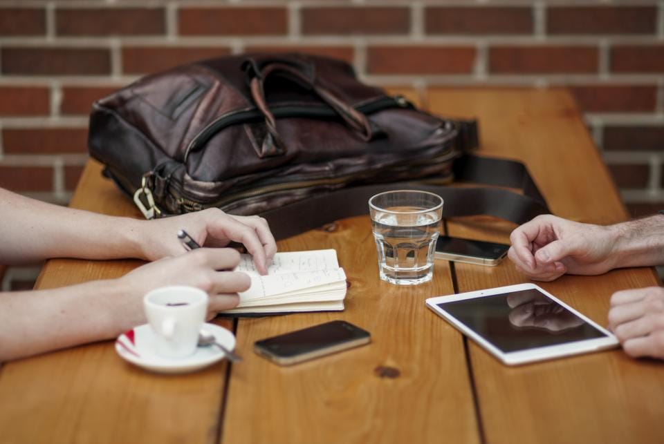 Two people at a meeting table with a notebook, tablet and coffee