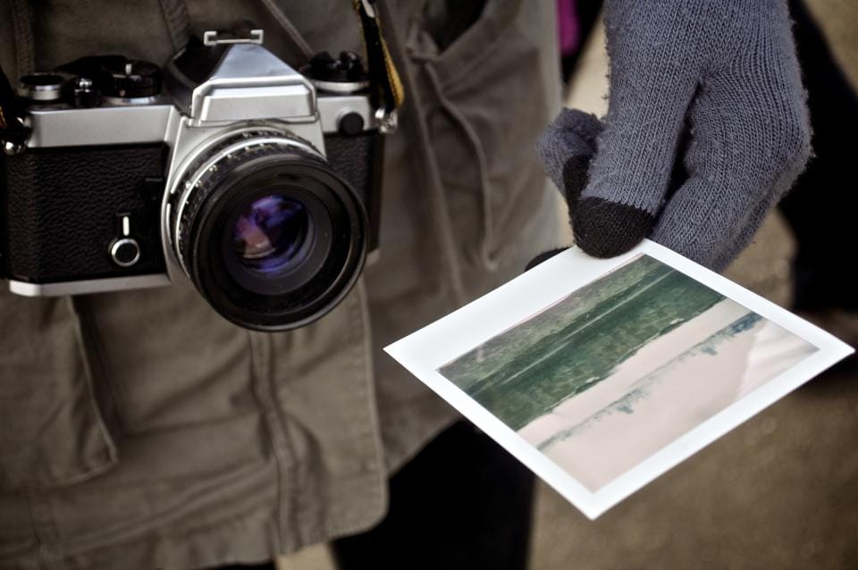 A film camera on a strap and a printed photo in a gloved hand