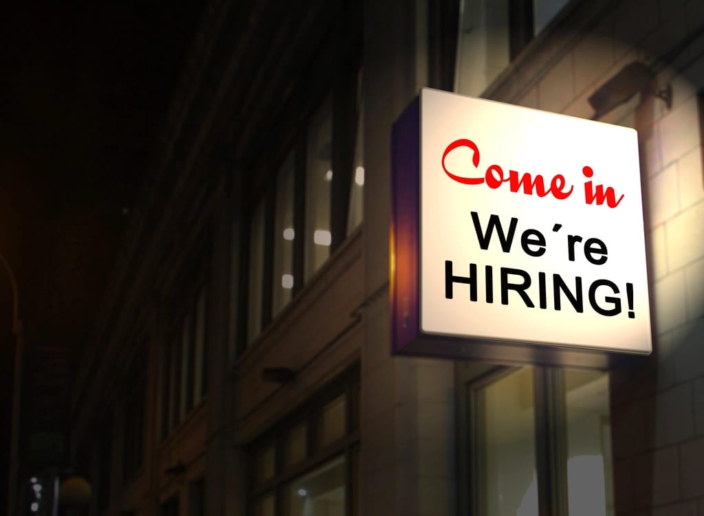 A lit sign on a building reading Come in, we are hiring
