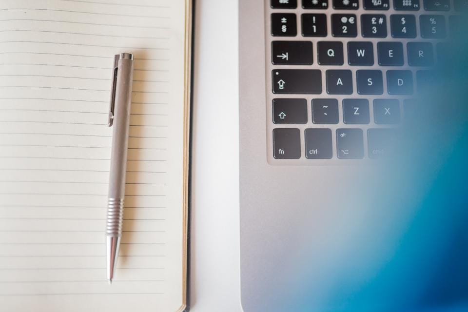 A pen on a lined notebook beside a laptop keyboard