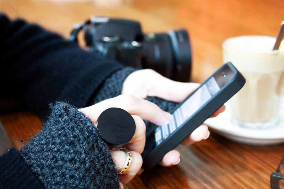 Hands scrolling a phone in a cafe, a camera on the table